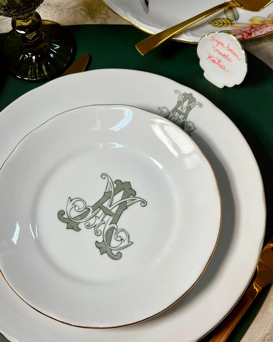 Pratos de porcelana com monograma verde e friso de ouro em mesa posta